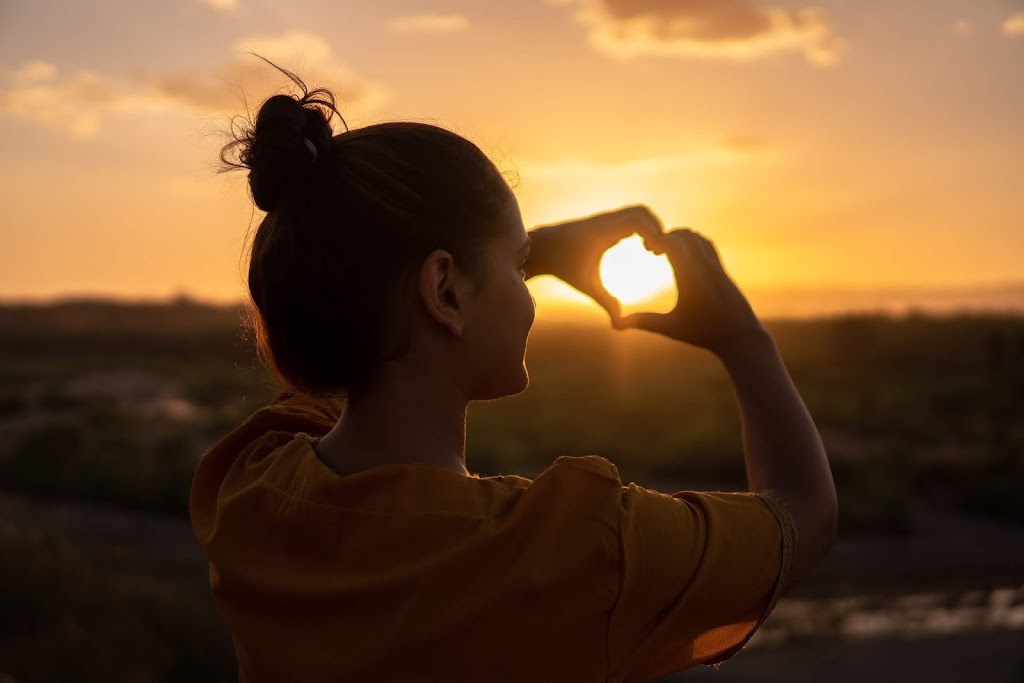 woman making heart with hands around sun