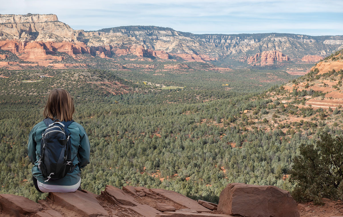 woman with backpack sitting on mountainside looking at view